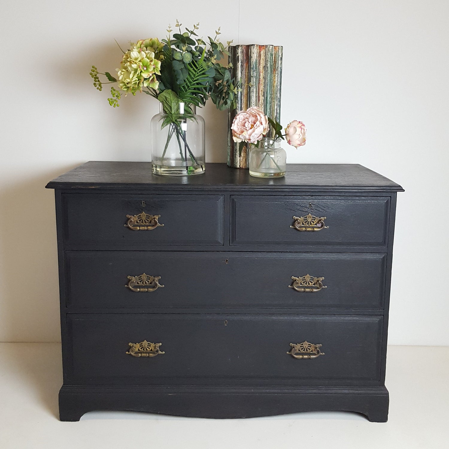 A beautiful antique wooden drawer dresser unit painted in a dark black wood stain with reclaimed golden antique handles on each drawer