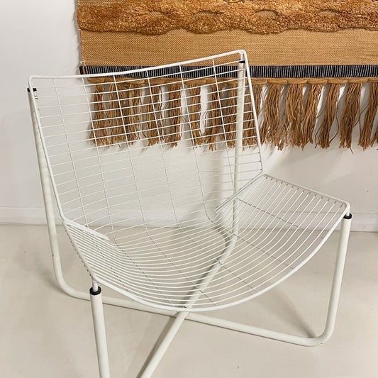 a vintage white Ikea Jarpen Chai, comes in a set of two. The chair has a tan brown wall hanging in the background