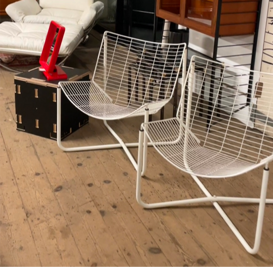 both chairs in the set are shown on an exposed hardwood floor with a ladderax unit in the background. The chairs are white wire mesh