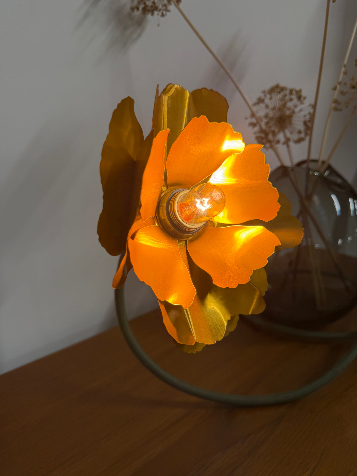 A flower lamp with its bulb lit on a vintage sideboard 