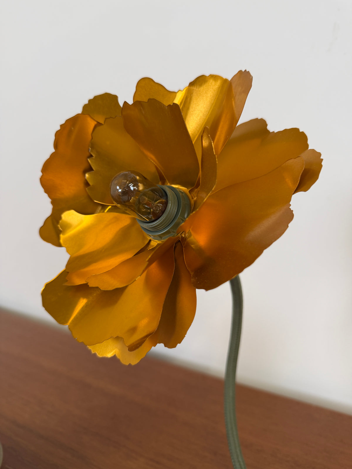 Flower lamp made from a gold coloured metal with a wire that is green and made to look like the stem
