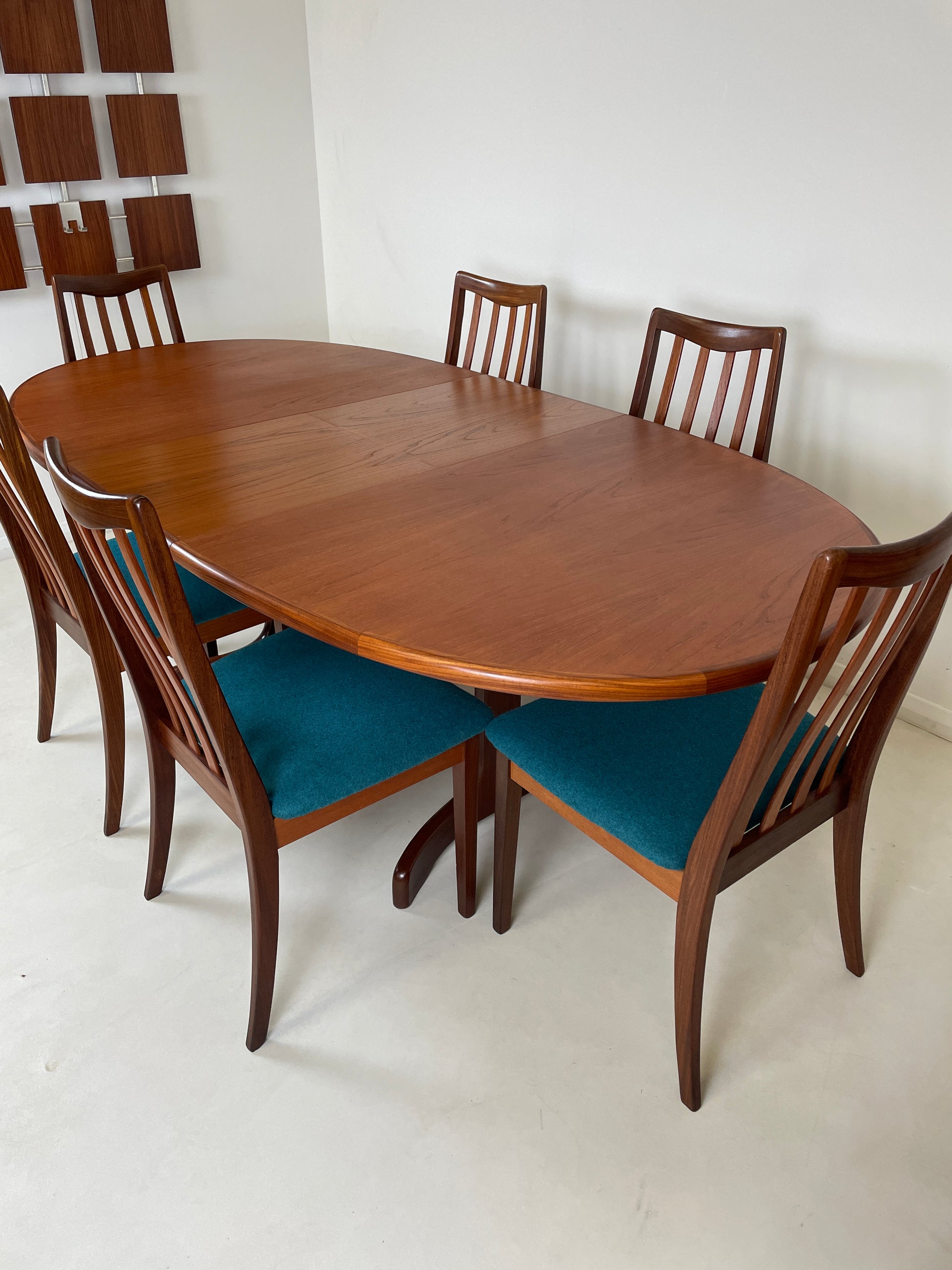 the table is in a white room with white floors, the table extends to fit more people around it & has been pulled out to fit a total of 6 chairs around it now. The seat of each chair is shown with the matching teal upholstered cushions on every one