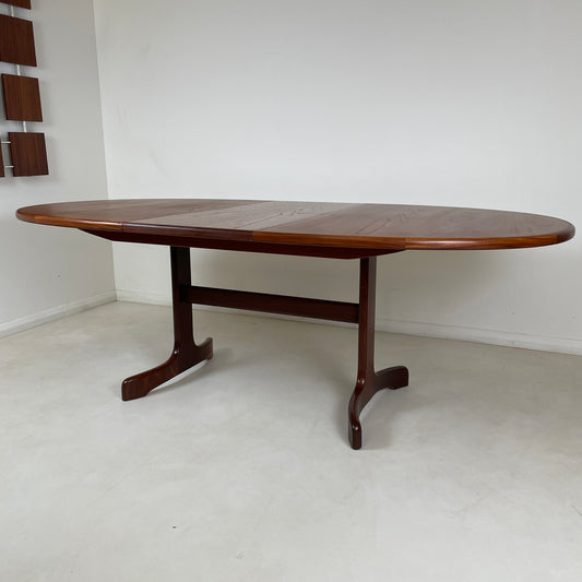 the table is shown by itself in the white room, the legs of the table are at either end with a section in the middle to support the extension of the table. It is an oval shaped table 