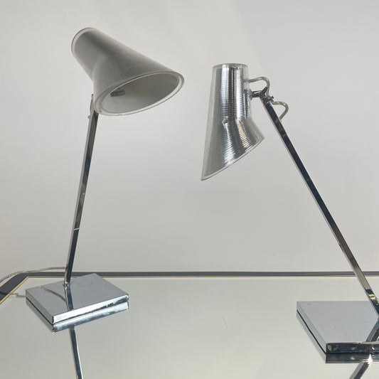 A glass table with the two lamps on top of the table. One of the lamps is at a downwards angles to show you can adjust where the light gos. The other lamp is forward facing. Both are silver and in excellent condition.