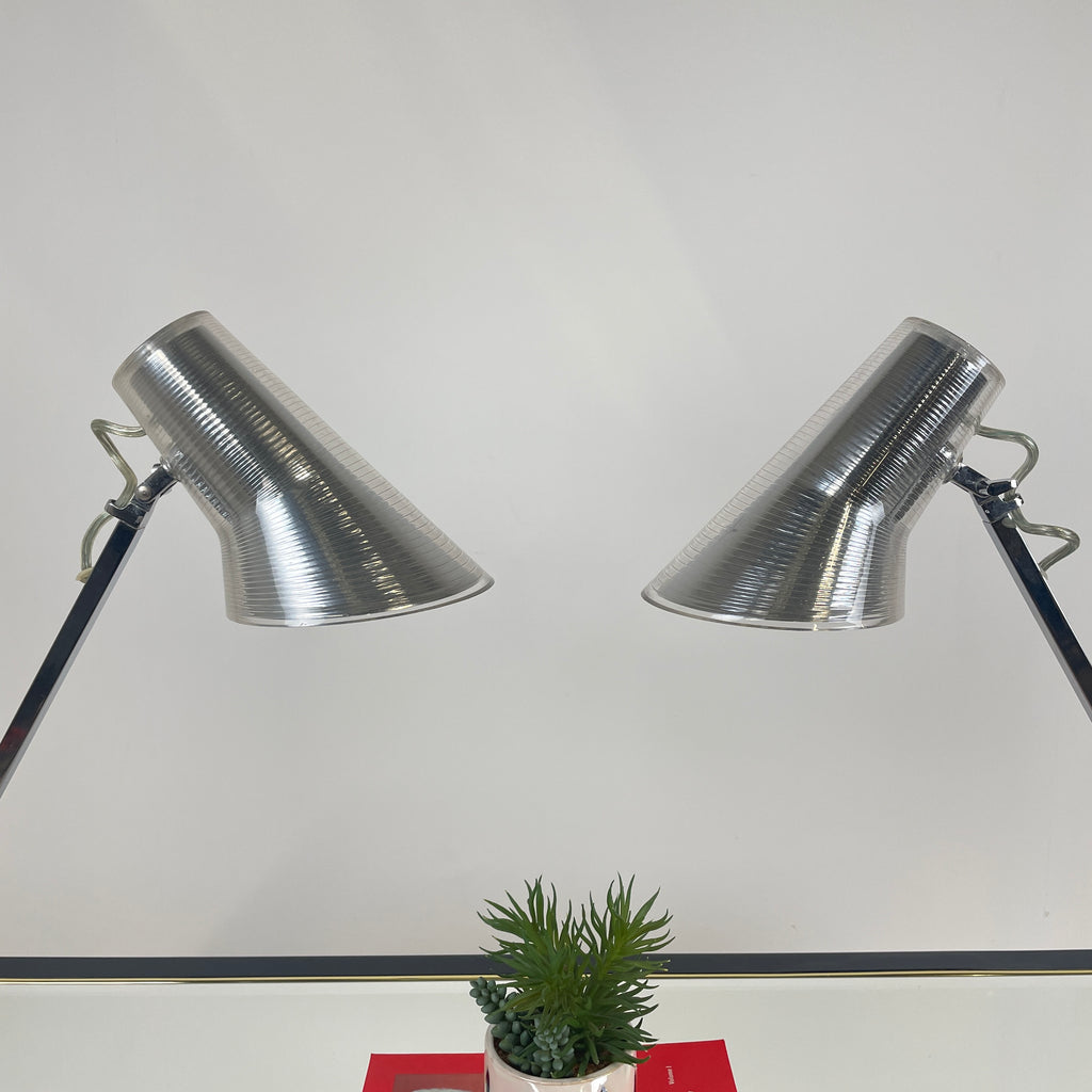the tops of both lamps where the bulbs go are shown facing down towards a potted succulent plant and a red art book. Their thin necks are shown too.