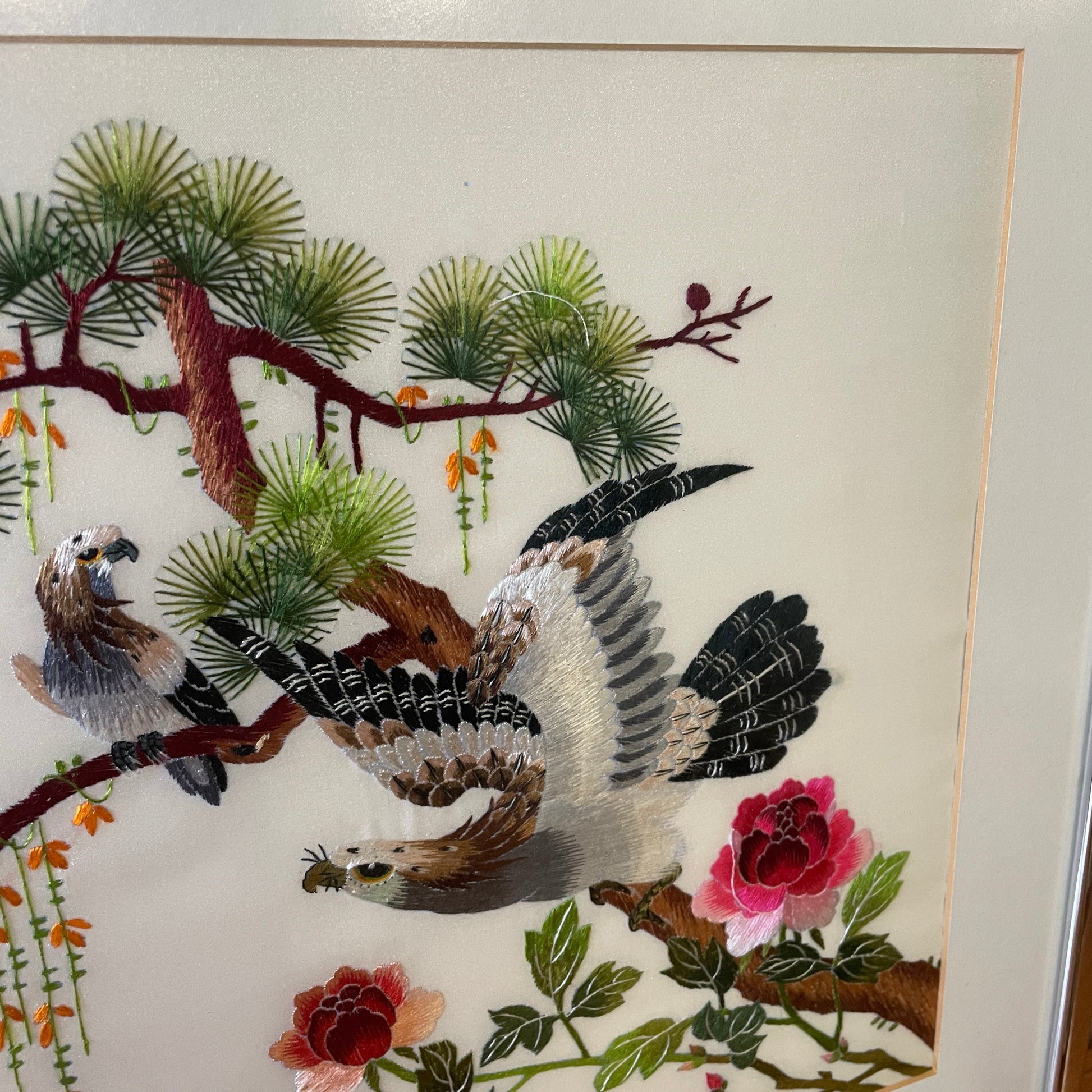 A closer image of the craftmanship of the embroidery, there are two embroidered eagles on branches of a tree, with two pink flowers and climbing orange floral and green leaves. 