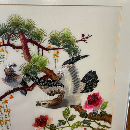 A closer image of the craftmanship of the embroidery, there are two embroidered eagles on branches of a tree, with two pink flowers and climbing orange floral and green leaves. 