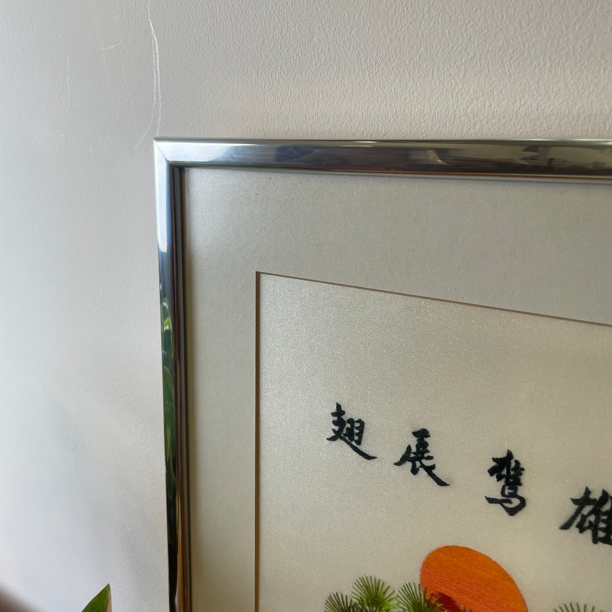 the silver frame with the off white grey mount and glass covering to protect the artwork shown against a white wall background.