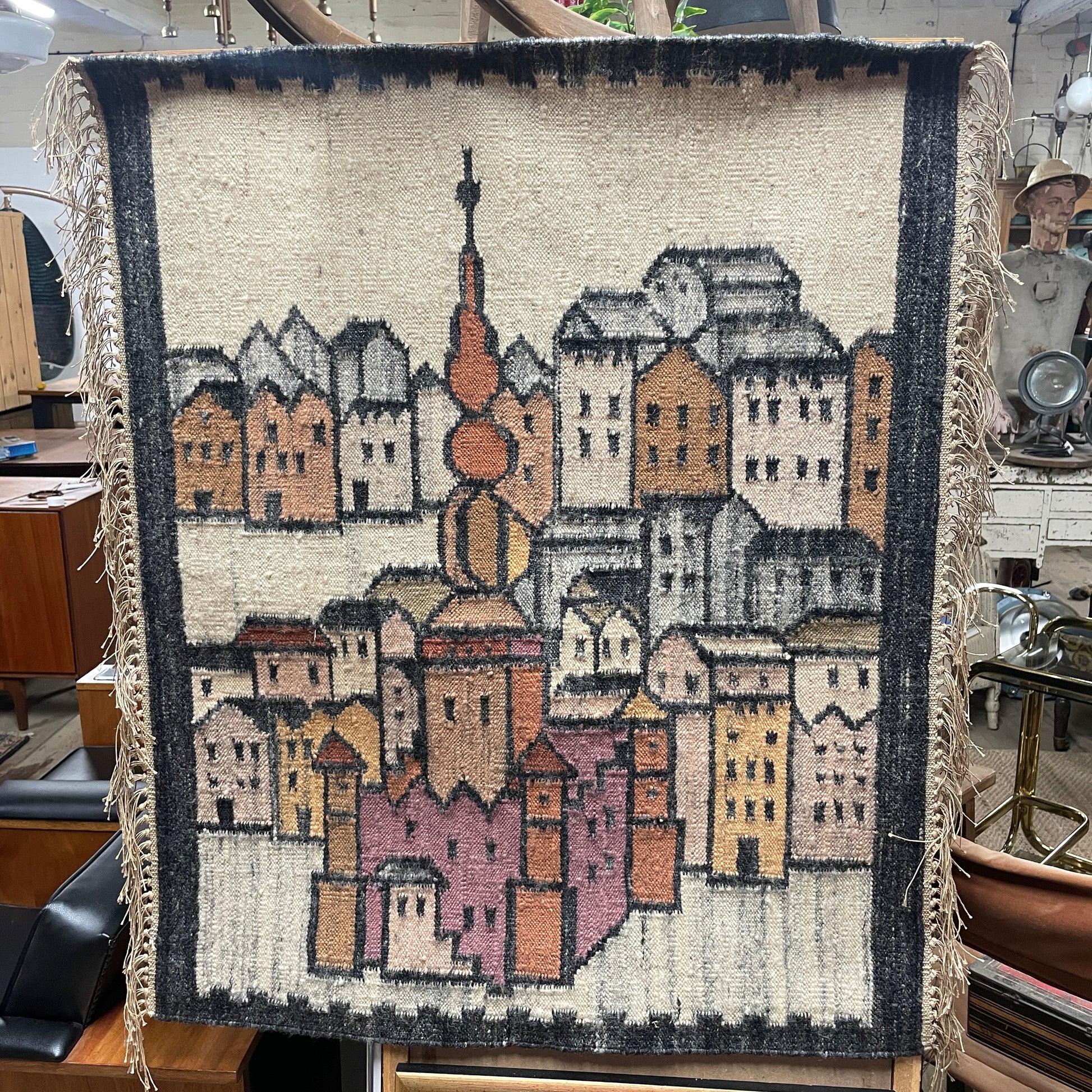 Vintage Decorative Egyptian Wool Wall Hanging , with cream fringed sides, the hanging is a weaved picture of a city landscape of a religious monument surrounded by high houses, in the style of L.S Lowry paintings. 