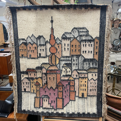 Vintage Decorative Egyptian Wool Wall Hanging , with cream fringed sides, the hanging is a weaved picture of a city landscape of a religious monument surrounded by high houses, in the style of L.S Lowry paintings. 